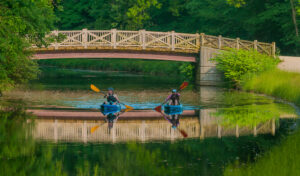 Photo by Mike Mitchell. Two kayakers paddle under a bridge on the canal. 