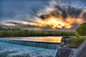 Print of bright sun peeking through dark clouds above Dam 5 by Margaret J Clingan